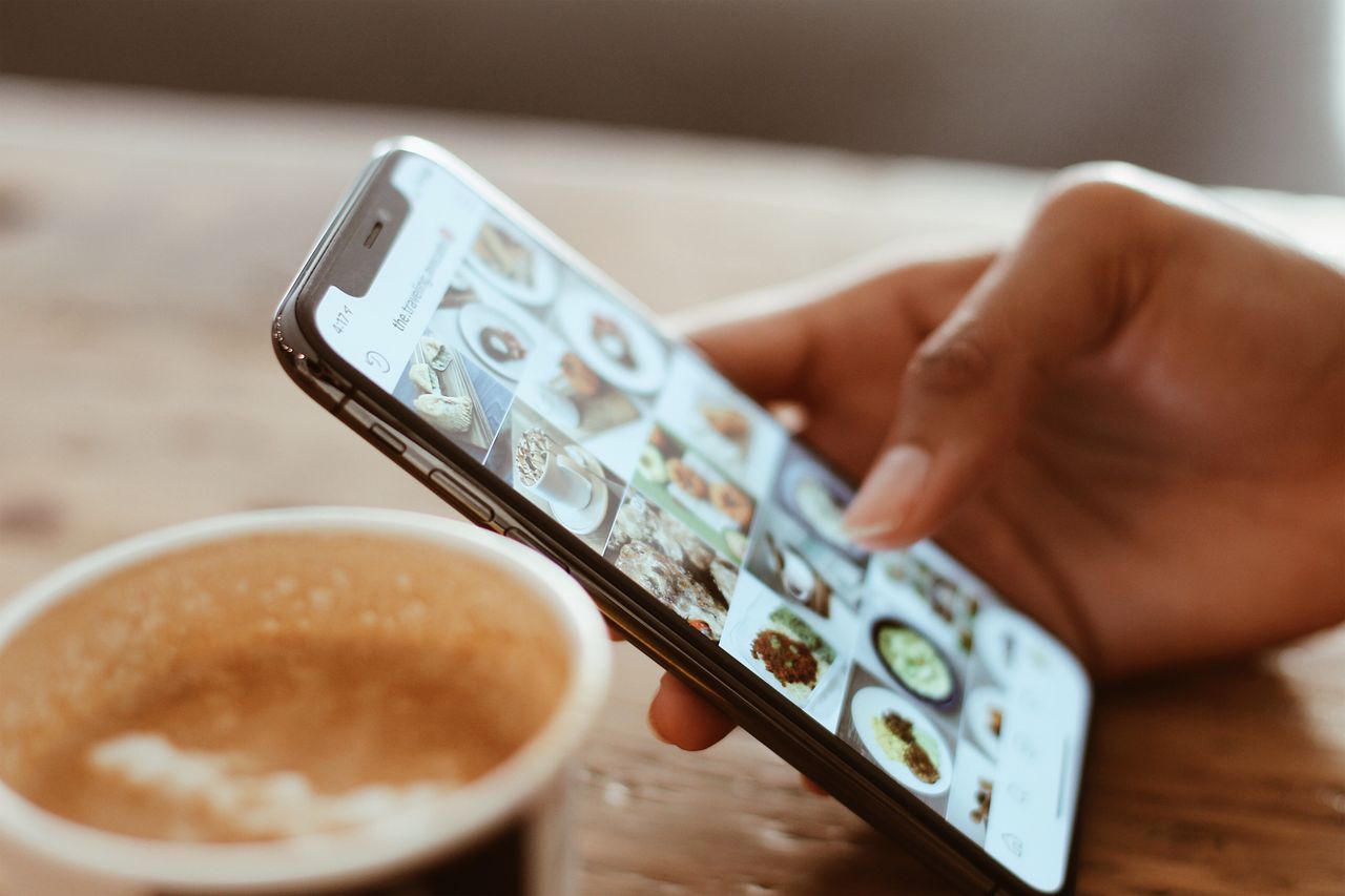 Hand browsing photos on an iPhone next to a cup of coffee
