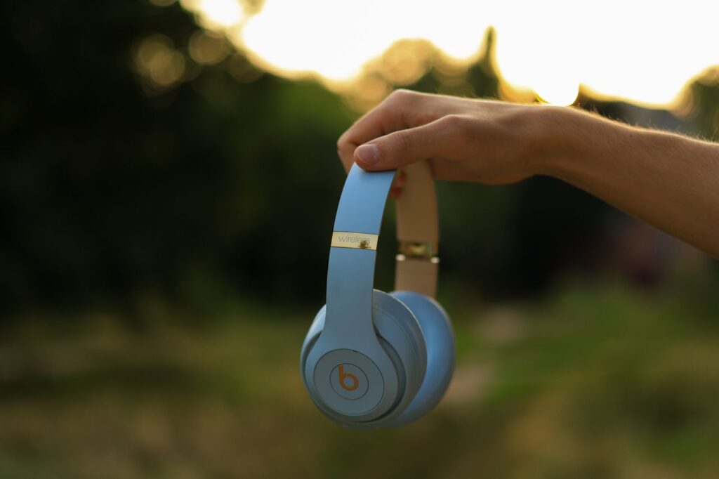 Hand holding blue wireless headphones outdoors at sunset
