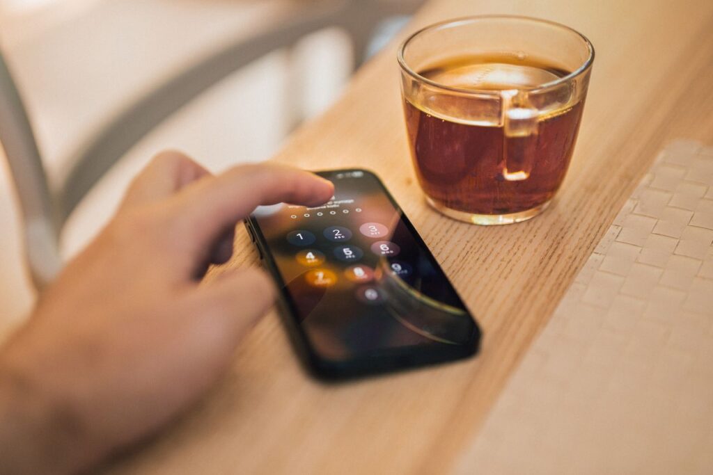 Hand unlocking a smartphone with a passcode next to a cup of tea