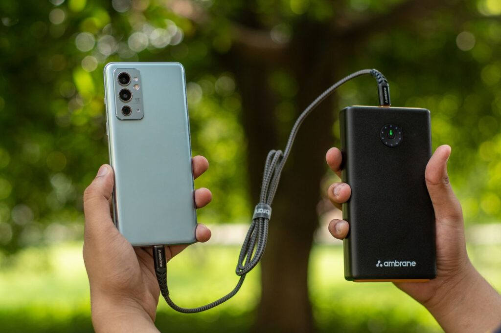 Hands holding a smartphone connected to a power bank outdoors