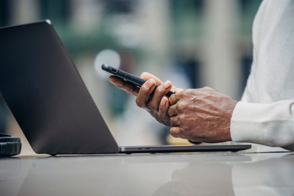 Man using a smartphone and laptop at an outdoor cafe