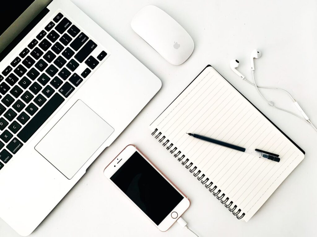 Minimal desk with laptop, smartphone, notebook and earbuds