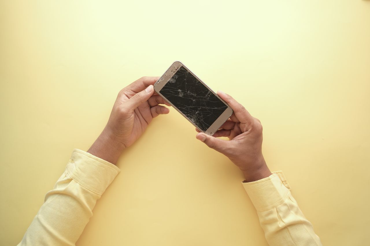 Person holding a smartphone with a broken screen