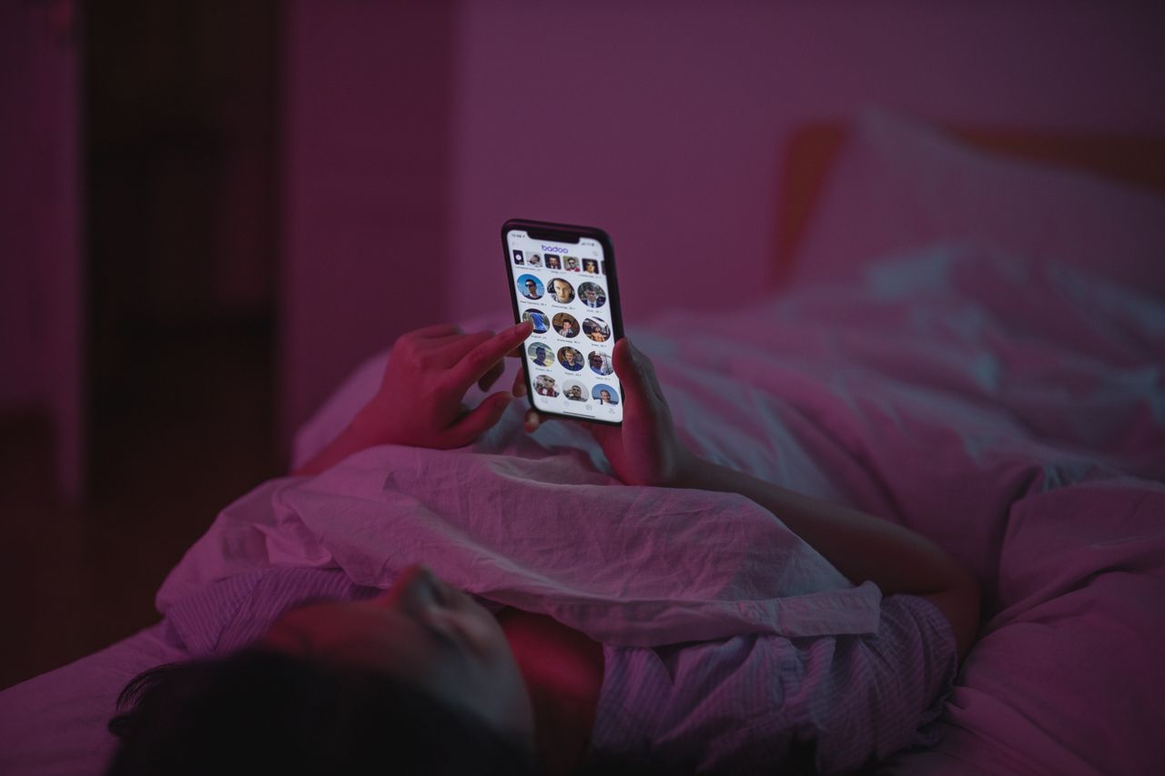 Woman relaxing in bed at night while using her iPhone