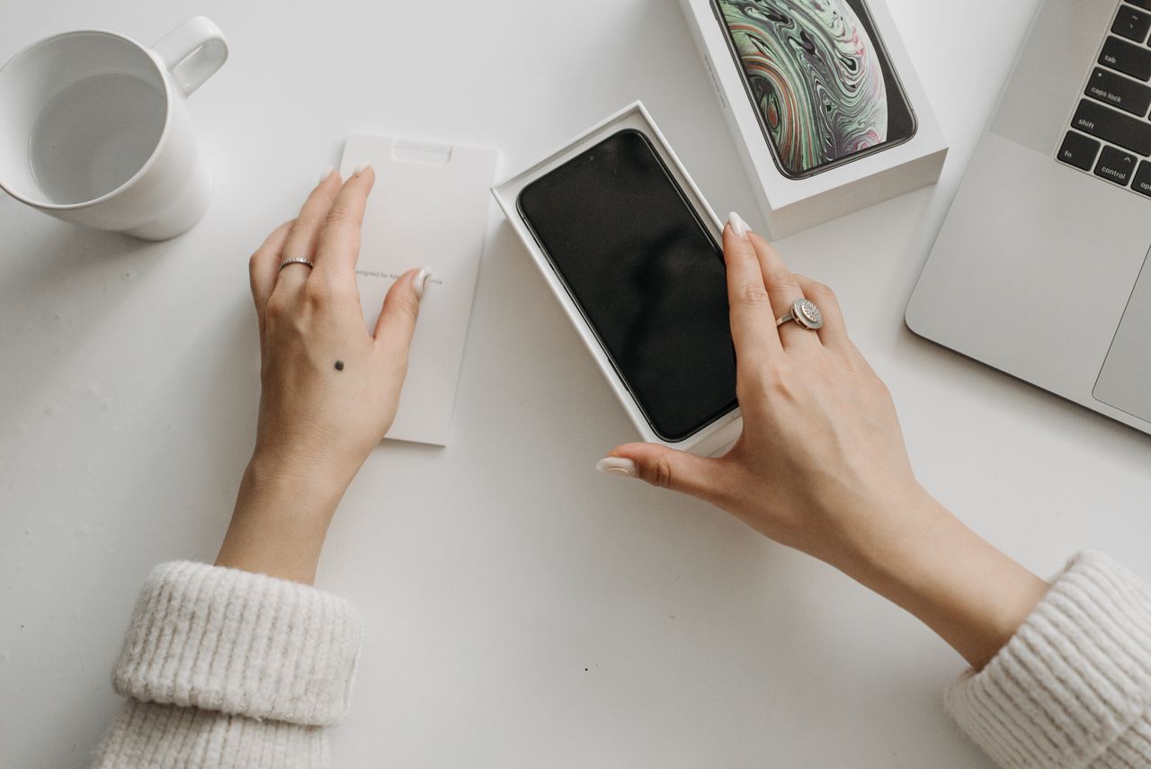 Woman unboxing a new smartphone on a white table