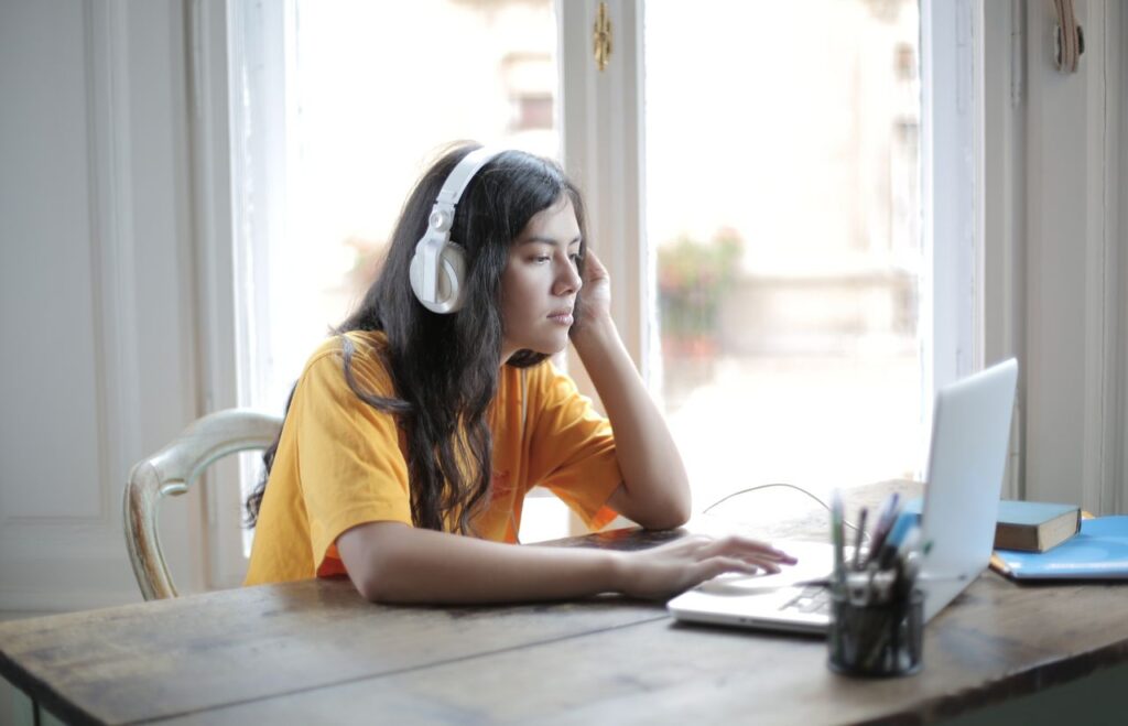 Woman with headphones listening to music while using a laptop
