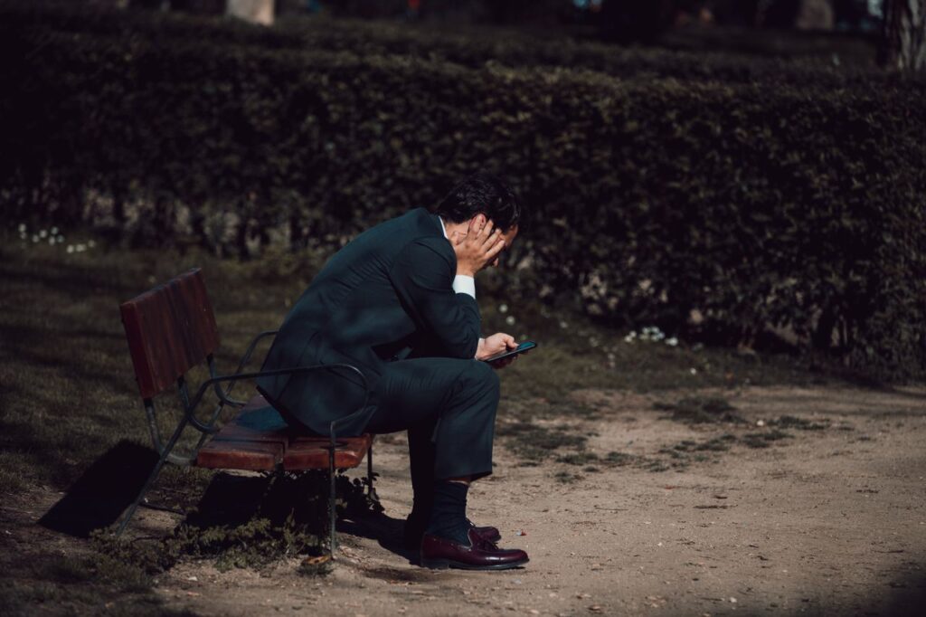 Worried man sitting with a smartphone in a park