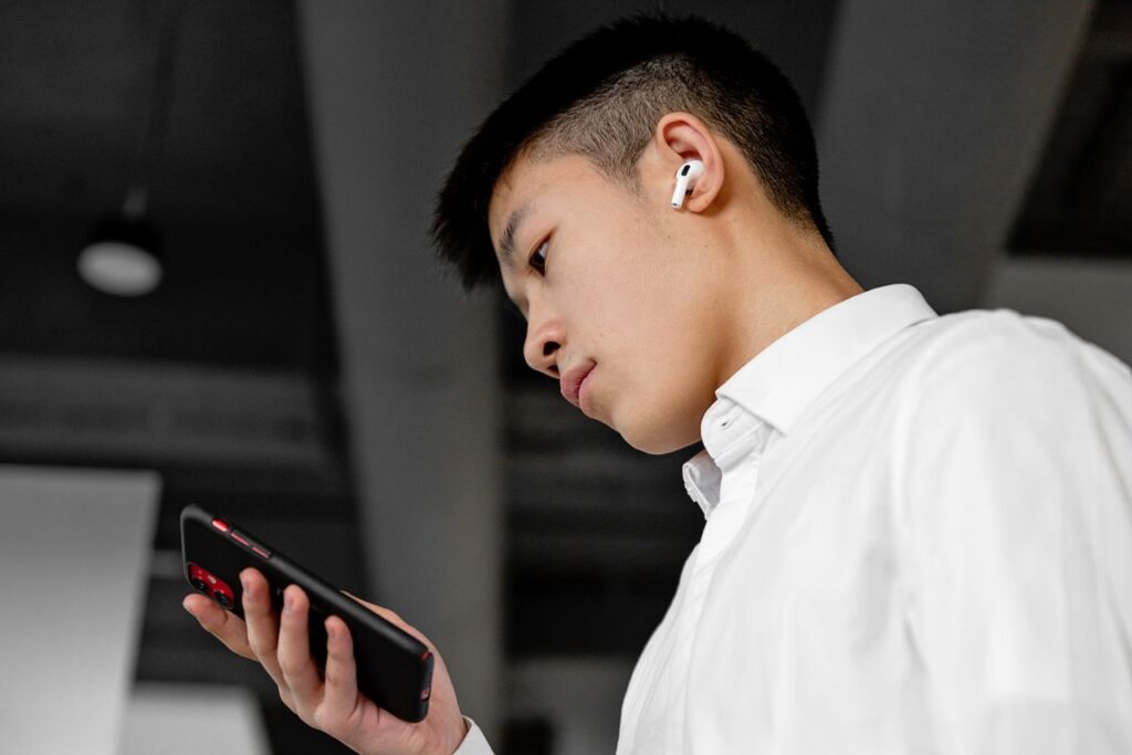 Young man wearing wireless earbuds and using a smartphone indoors