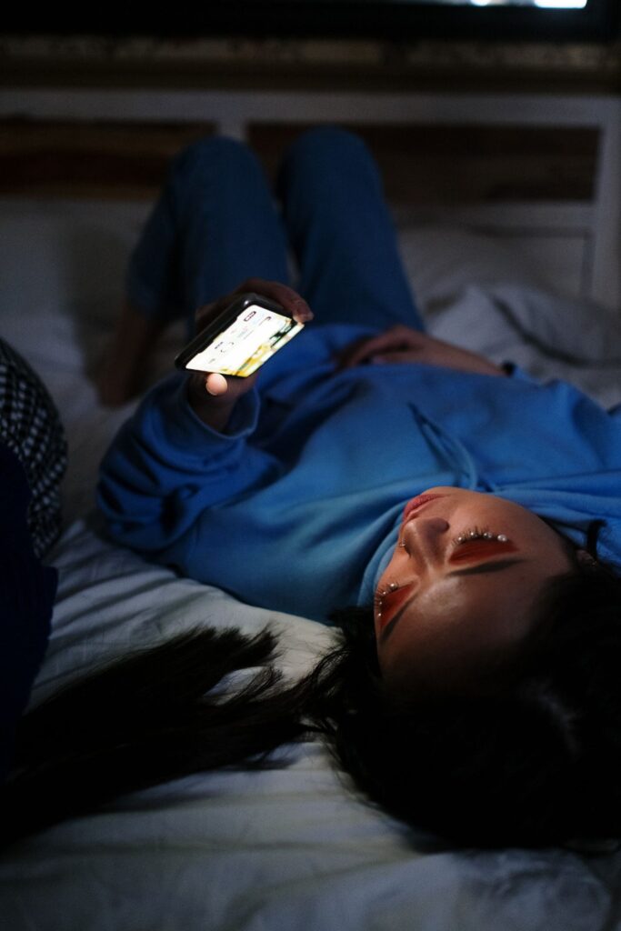 Young woman lying on a bed looking at her phone in a dim room